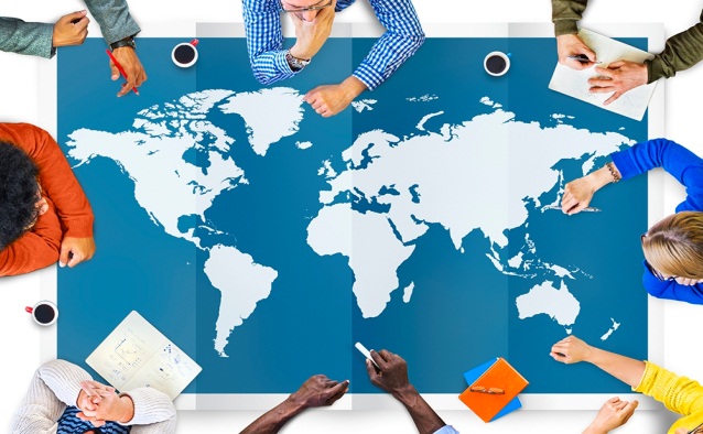 Table covered with a map of the globe, surrounded by people working