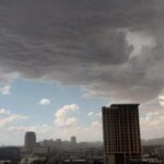 Dark storm clouds encroach on a blue sky over the downtown Phoenix skyline, mountains in the background