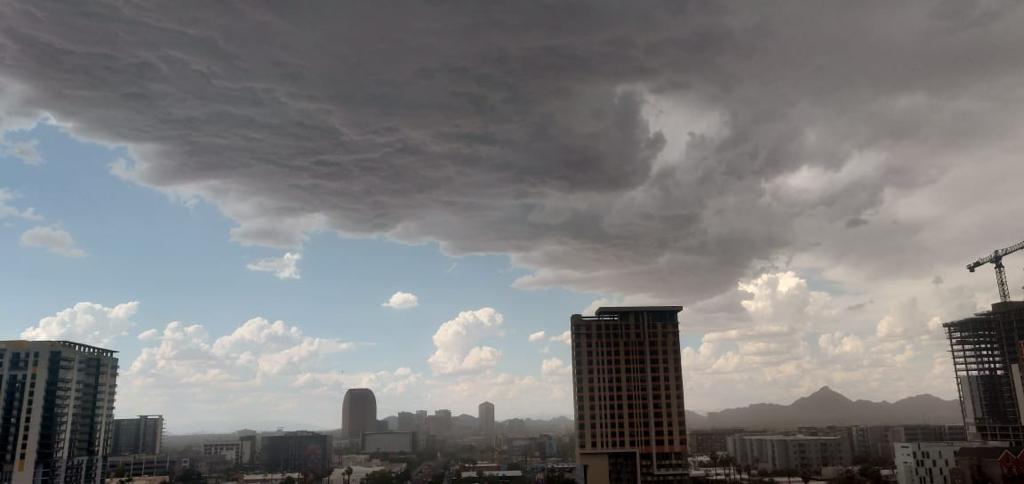 Dark storm clouds encroach on a blue sky over the downtown Phoenix skyline, mountains in the background