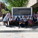 17 Media scholars, educators, and professionals pose in front of a stone tablet bearing the ASU charter on the downtown campus