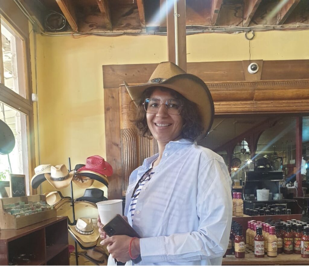 A smiling Scholar stands in a shop, wearing a Western hat