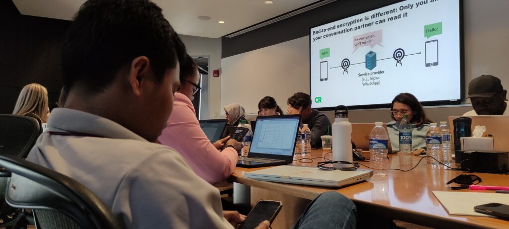 The scholars examine their devices while Yael Grauer lectures on cybersecurity for journalists