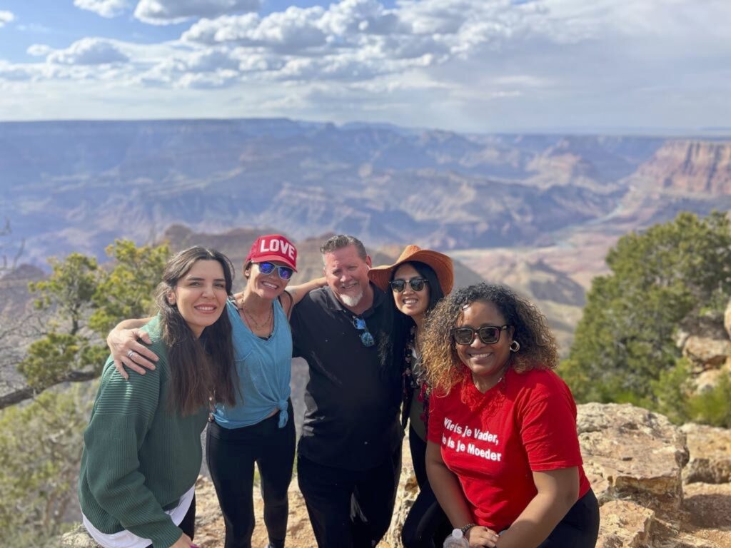 A group of smiling people stands in front of the Grand Canyon