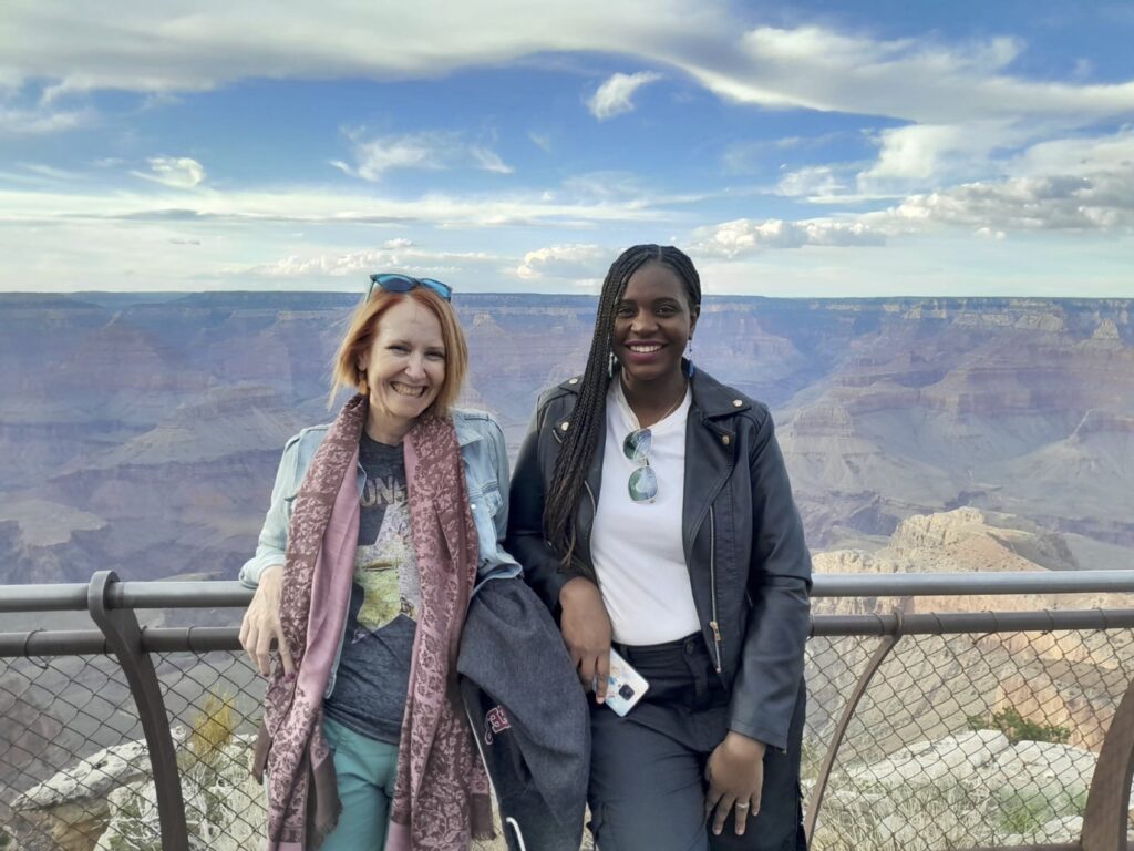 Two women stand leaning against a railing in front of the vast expanse of the Grand Canyon