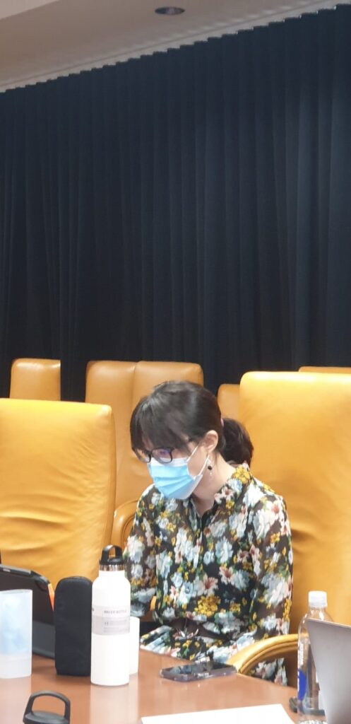 A young woman sits at a conference table, concentrating on her tablet