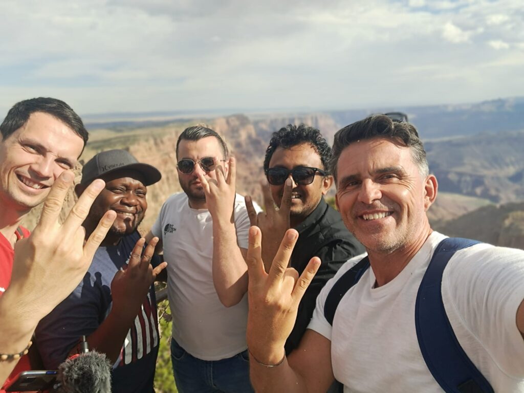 Five scholars gesture at the camera against the backdrop of the Grand Canyon