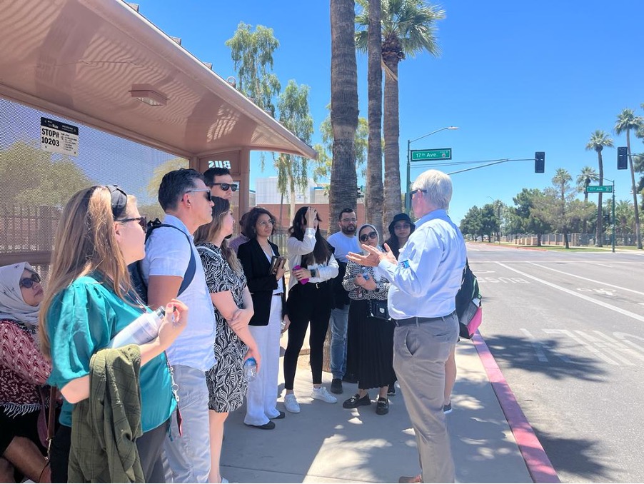 The scholars and Dan Barr chat at a bus stop in central Phoenix