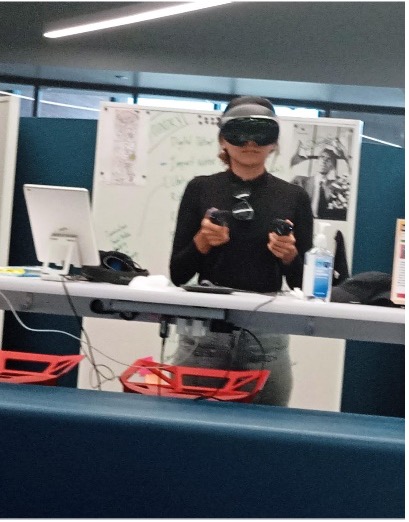 A woman wearing a VR headset manipulates two hand controllers