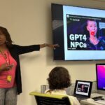 Retha Hill points to a screen with a video illustration of AI tools, while the scholars observe