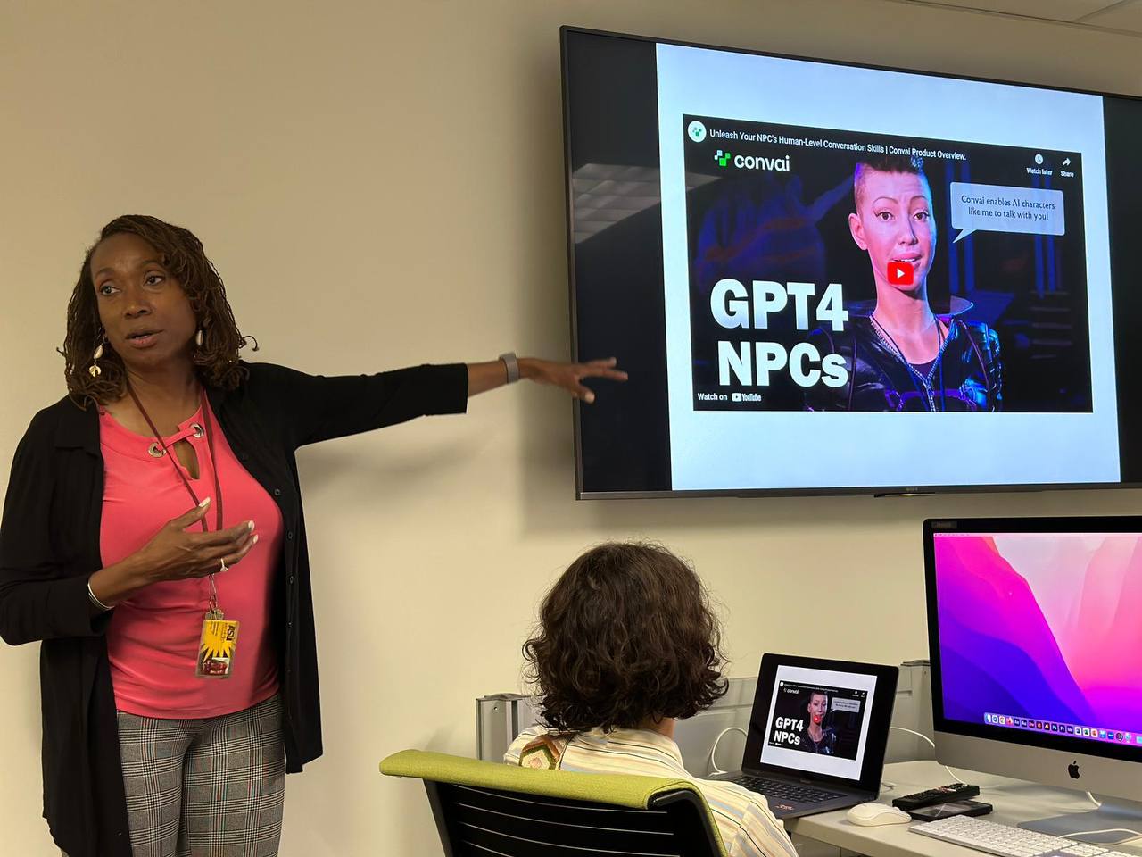 Retha Hill points to a screen with a video illustration of AI tools, while the scholars observe