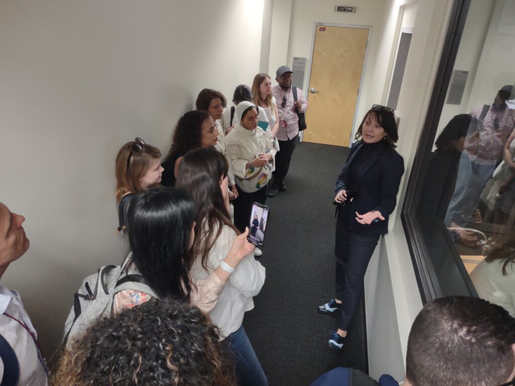 Scholars line the hallway outside the Cronkite News control room while Executive Editor Christina Leonard explains the process to them