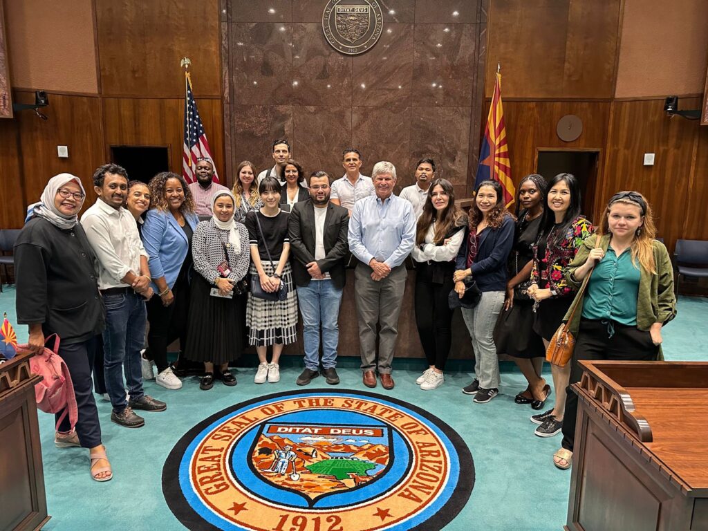 The scholars pose for a group shot in the Arizona House chamber, around the official state seal