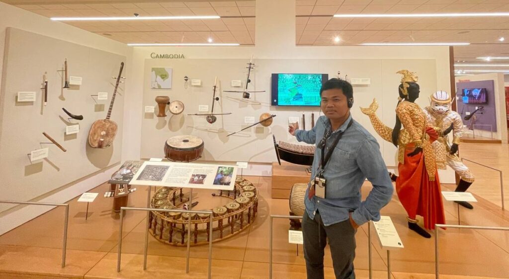 A Cambodian scholar proudly pointing to the exhibit of instruments from his home country