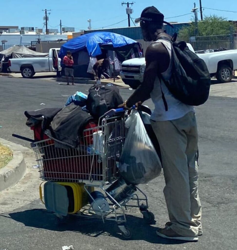 A black man pushes a shopping cart filled with belongings