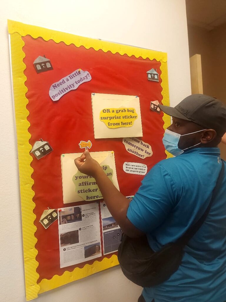 Scholar Elastus Mambwe of Zambia stands in front of a positivity bulletin board at the CASS shelter, ready to affix a sticker that reads "Hope"