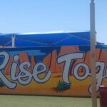 A mural reads "We Rise Together," with desert images and a saguaro cactus