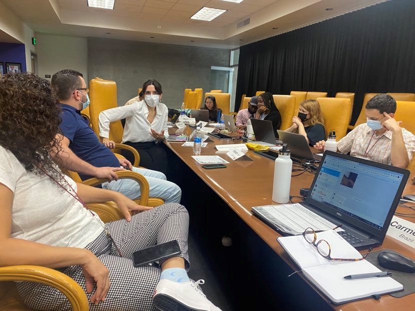 The scholars engage in discussion around the conference table in 444