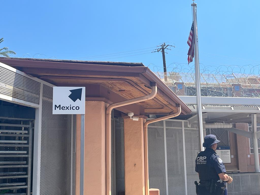 A border guard stands at the crossing station, with a sign pointing toward Mexico