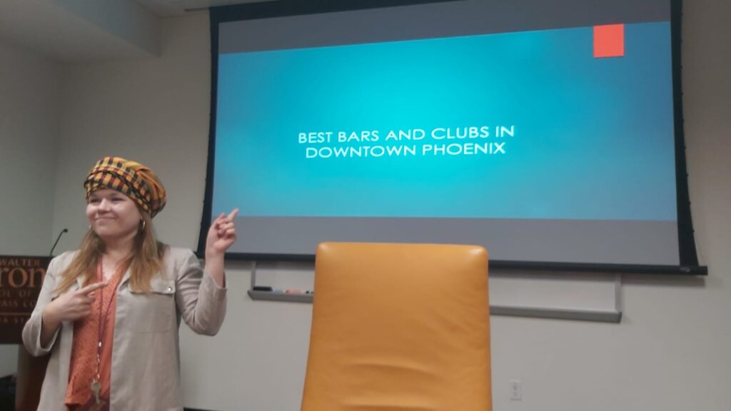 A scholar stands in front of a slide labeled "Best Bars and Clubs in Downtown Phoenix" as a joke before discussing her actual project