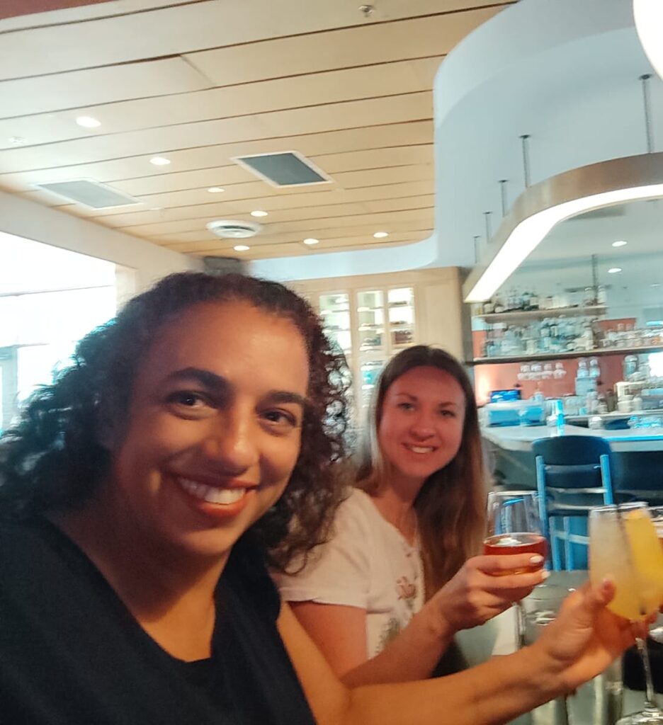 Two women hold up drinks in a toast to the camera