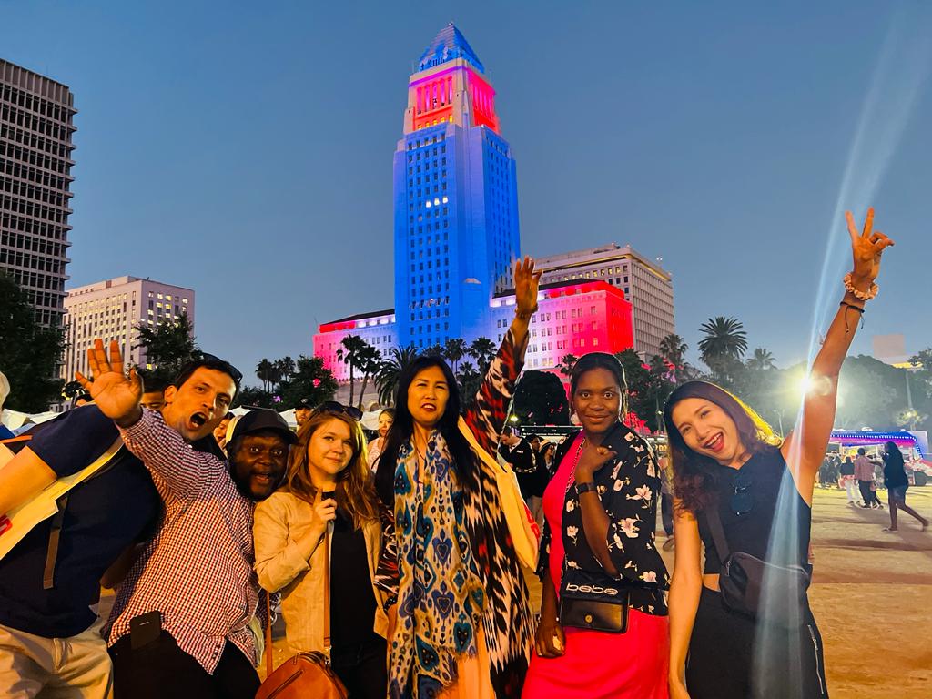 A group of scholars stands in front of a building illuminated in red, white and blue at dusk