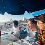 Three scholars sit at a dining table overlooking the coast