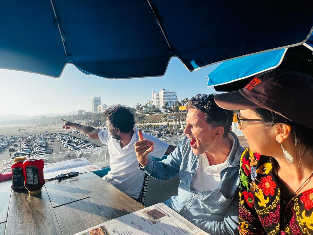 Three scholars sit at a dining table overlooking the coast