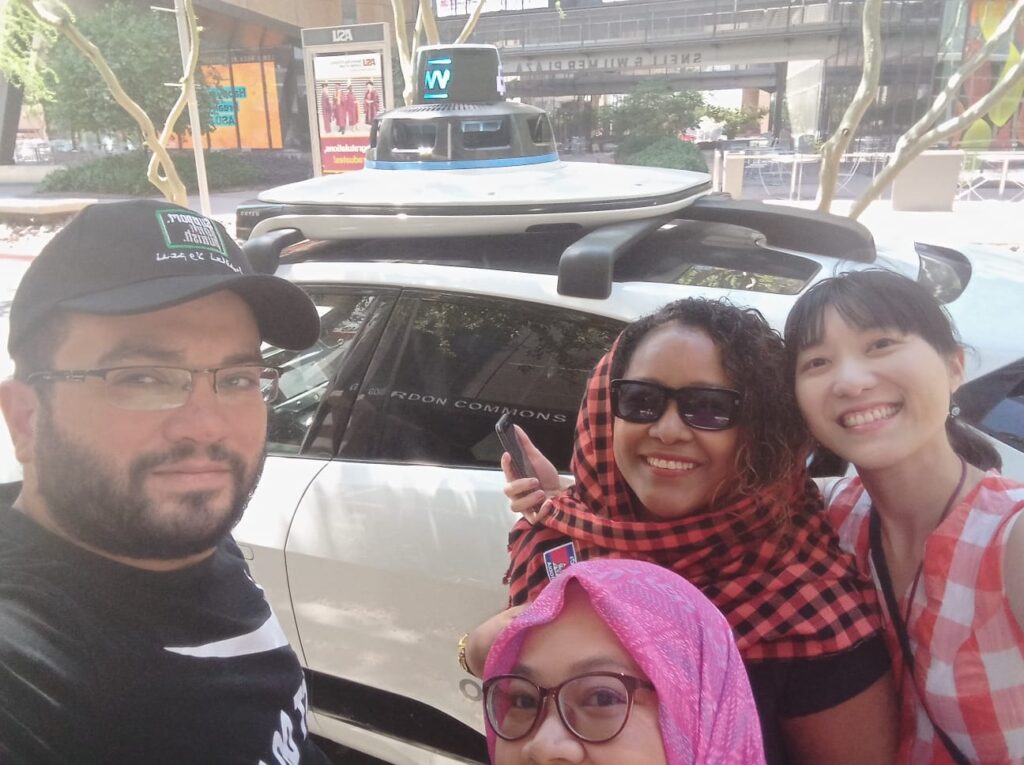 Four scholars are pictured in front of a Waygo driverless taxicab