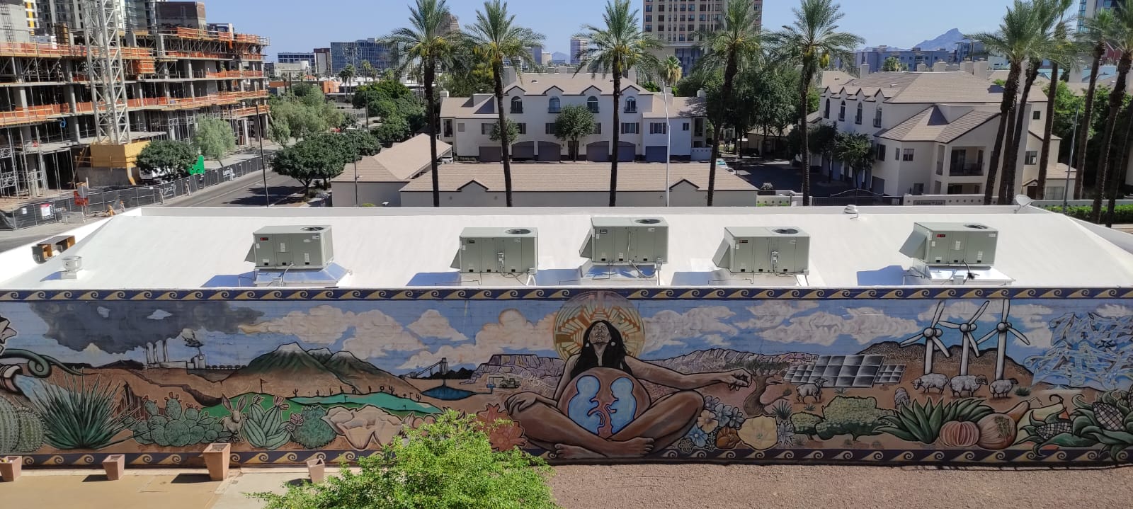 View of a small city park with a mural by Indigenous artists depicting Mother Earth in the desert