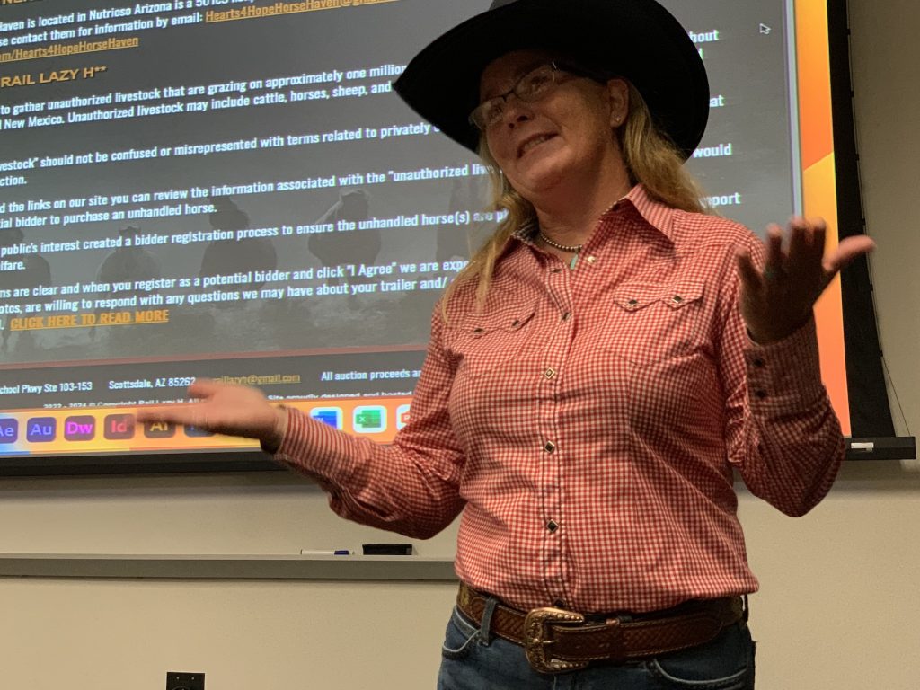 A woman in a plaid shirt and black cowboy hat stands in front of a projector slide