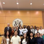 The scholars pose for a group photo in a U.S. district courtroom, in front of an American flag and the US District Court seal