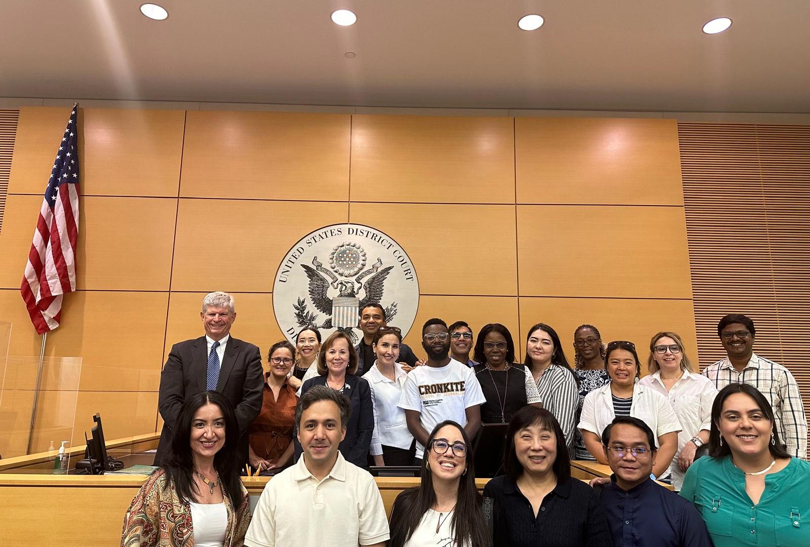 The scholars pose for a group photo in a U.S. district courtroom, in front of an American flag and the US District Court seal