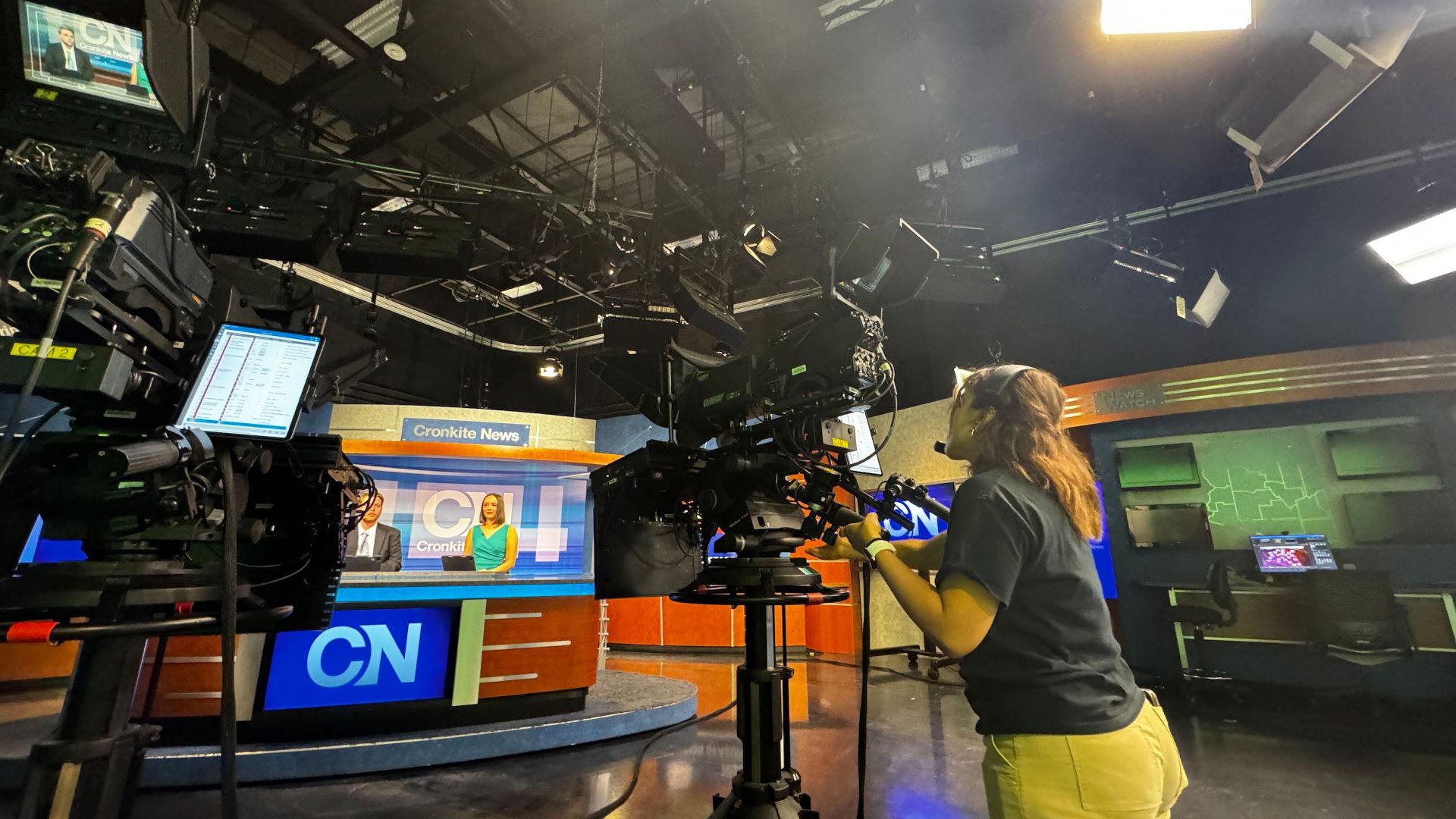 The Cronkite News studio during a newscast, with student anchors at the desk and another student operating the camera in the foreground