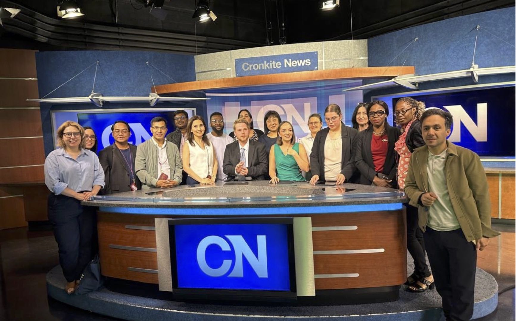 The scholars pose behind the Cronkite News anchor desk