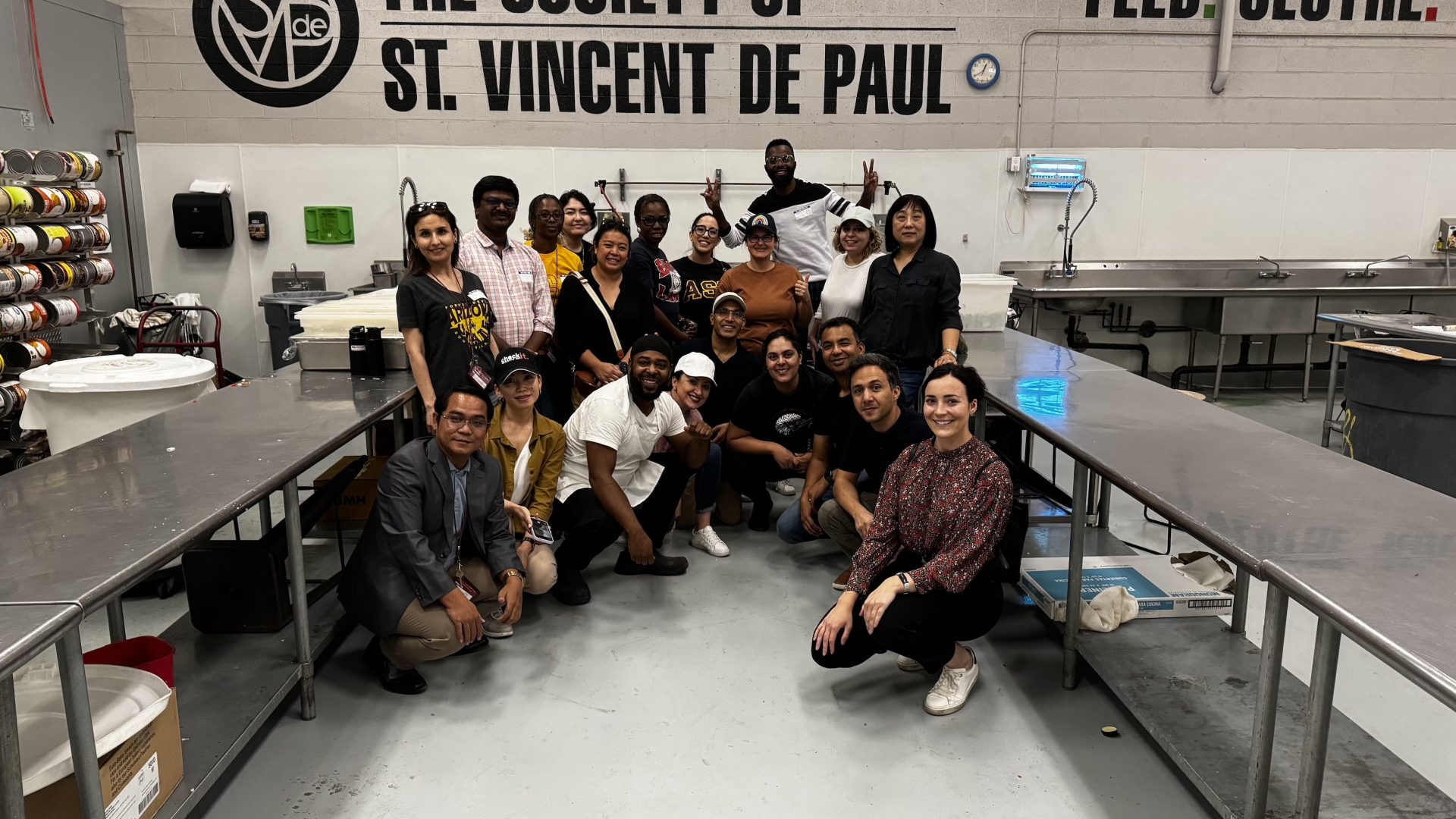 The scholars and Kate Devine pose in a clean industrial kitchen under the logo of the Society of St. Vincent De Paul