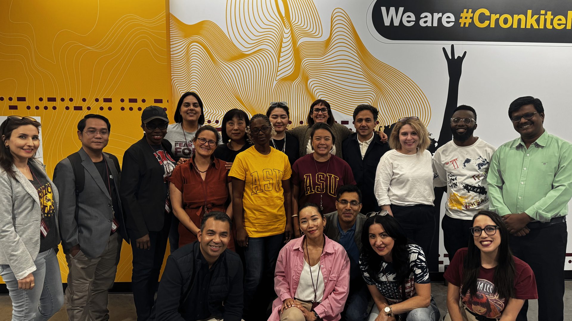 The scholars pose for a group photo in front of the 4th floor mural, under a sign reading "We are #CronkiteNation"