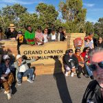 The scholars (with bus driver Ronnie in the foreground) pose around the stone sign marking Grand Canyon National Park