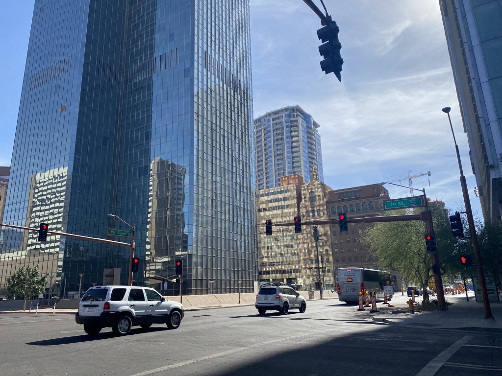 Tall, modern buildings, wide roads, and a blue sky reflected in dozens of office windows